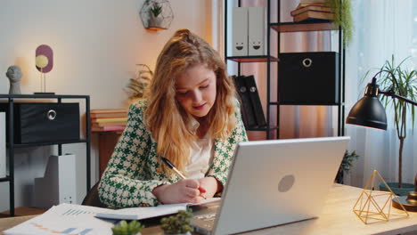 Business-woman-writing-down-taking-down-notes-while-attending-online-video-class-meeting-on-laptop