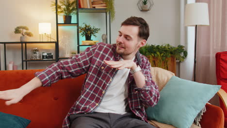 Man-singing-and-dancing-celebrate-victory-win-enjoying-music-sitting-on-couch-in-living-home-room