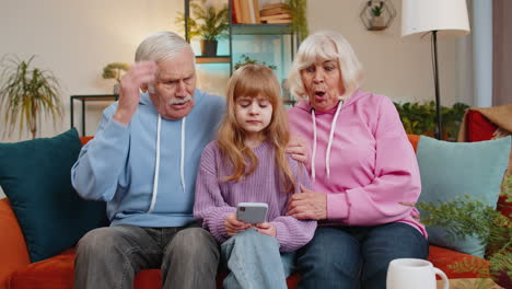 Niña-Nieta-Abuelo-Abuela-Jugando-En-El-Teléfono-Inteligente-Perdiendo-Falla-En-Casa