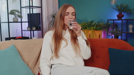 Thirsty-one-young-woman-sitting-at-home-holding-glass-of-natural-aqua-make-sips-drinking-still-water