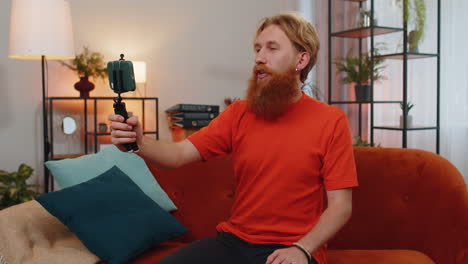 Bearded-man-blogge-taking-selfie-on-smartphone-communicating-video-call-home-online-with-subscribers