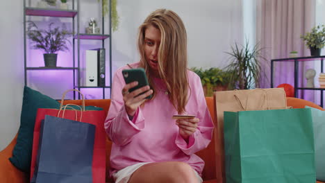 Happy-shopaholic-young-woman-sitting-with-shopping-bags-making-online-payment-with-credit-card