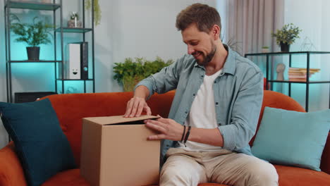 Happy-young-man-shopper-unpacking-cardboard-box-delivery-parcel-online-shopping-purchase-at-home