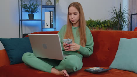 Smiling-happy-girl-counting-money-cash-and-use-laptop-pc-calculate-domestic-income-earnings-at-home