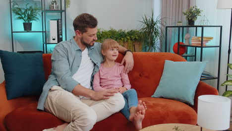 Young-man-father-having-trustworthy-conversation,-talking-with-daughter-child-kid-at-home-sofa