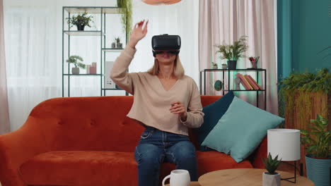 Una-Mujer-Joven-Usa-Gafas-De-Realidad-Virtual-En-Casa,-Disfrutando-Del-Concepto-De-Vídeo-Moviendo-Las-Manos-En-El-Aire