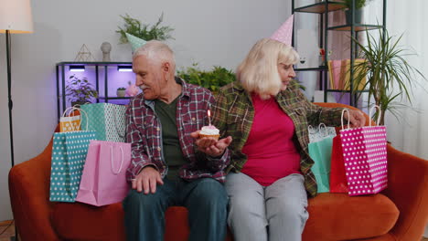 Happy-senior-family-man-woman-celebrating-birthday-anniversary-hold-cupcake-makes-wish-at-home