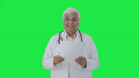 Happy-Indian-senior-doctor-reading-reports-Green-screen