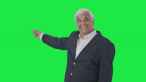 Happy-Indian-senior-journalist-pointing-at-green-screen-and-reading-news