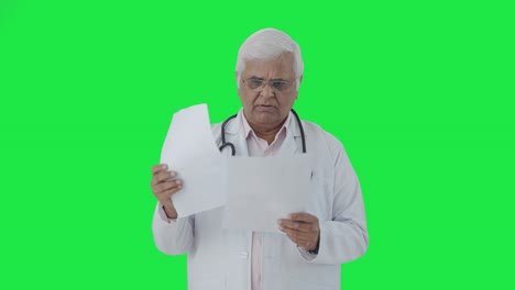 Indian-senior-doctor-reading-reports-Green-screen