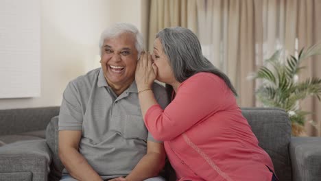 Happy-Indian-old-wife-telling-a-secret-to-her-husband-in-ear