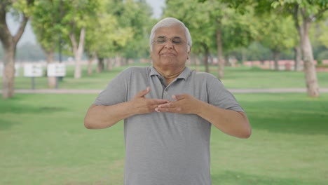 Relaxed-Indian-old-man-doing-breathe-in-breathe-out-exercise-in-park