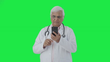 Médico-Senior-Indio-Desplazándose-Por-La-Pantalla-Verde-Del-Teléfono