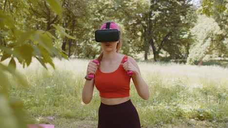 Athletic-girl-in-VR-headset-helmet-making-fitness-workout-boxing-exercises-with-dumbbells-in-park