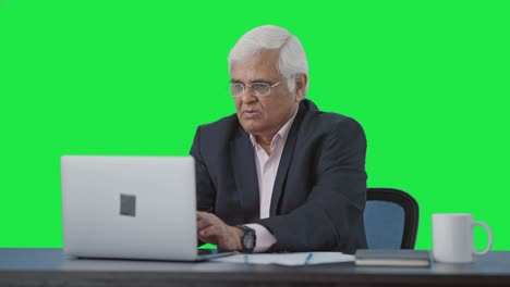 Serious-senior-Indian-manager-working-on-laptop-Green-screen