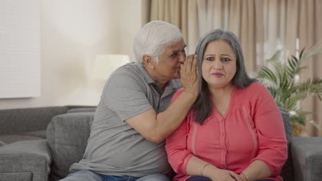 Happy-Indian-old-husband-telling-a-secret-to-his-wife-in-ear