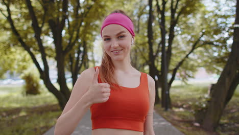 Portrait-of-athletic-smiling-runner-girl-looking-at-camera,-raises-thumbs-up-agrees-with-something