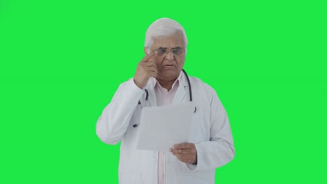 Confused-Indian-senior-doctor-reading-reports-Green-screen