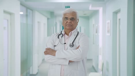 Confident-Indian-senior-doctor-standing-crossed-hands