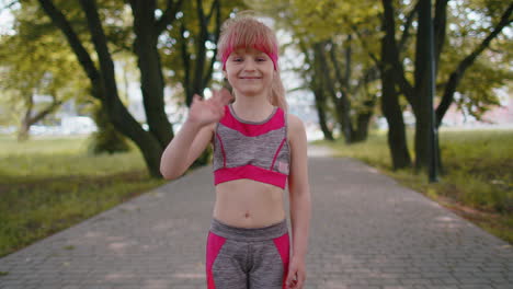 Athletic-fitness-toddler-runner-girl-waving-hi-with-her-palm-greeting-with-hospitable-friendly-smile