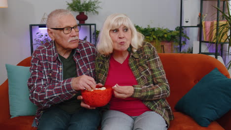 Pareja-De-Ancianos-Abuelos-Hombre-Mujer-Viendo-Una-Interesante-Película-De-Fútbol-En-Televisión,-Comiendo-Palomitas-De-Maíz