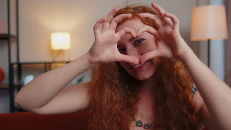 Redhead-young-woman-makes-symbol-of-love,-showing-heart-sign-to-camera,-express-romantic-feelings