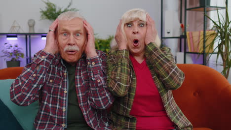 Wow,-excited-amazed-senior-old-man-woman-raising-hands-in-surprise-looking-at-camera-with-big-eyes