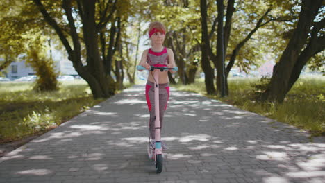 Young-athletic-fit-blonde-girl-rides-traveling-on-electric-scooter-on-road-in-park-on-sunny-day