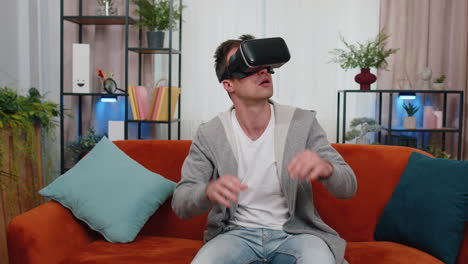 Young-man-use-virtual-reality-headset-glasses-at-home,-enjoying-video-concept-moving-hands-in-air