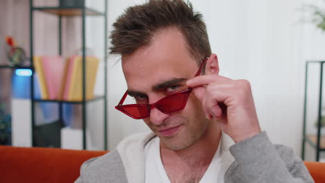 Seductive-cheerful-stylish-man-wearing-red-sunglasses,-charming-smile,-blinking-winking-eye-flirting