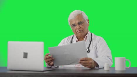 Indian-senior-doctor-reading-health-reports-Green-screen