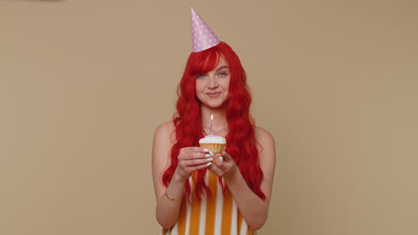 Happy-redhead-girl-celebrating-birthday-anniversary-party,-blowing-candle-on-small-cake-cupcake