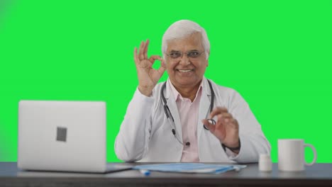 Happy-Indian-senior-doctor-showing-okay-sign-Green-screen