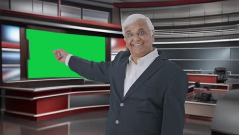 Happy-Indian-senior-journalist-pointing-at-green-screen-and-reading-news