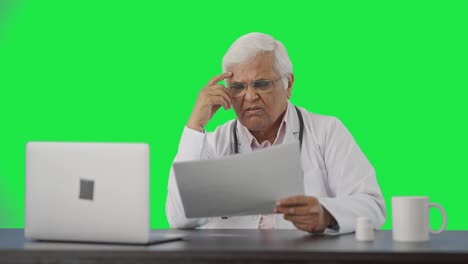 Tensed-Indian-senior-doctor-reading-health-reports-Green-screen