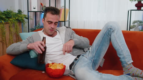 Hombre-Sentado-En-El-Sofá-Comiendo-Patatas-Fritas-Y-Viendo-Interesantes-Series-De-Televisión,-Partidos-De-Fútbol-En-Línea-En-Casa