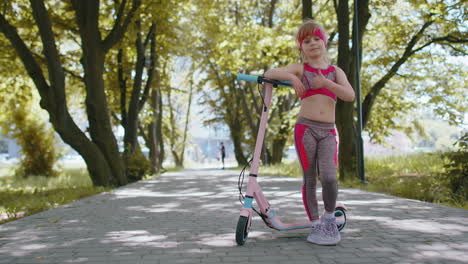 Young-athletic-fit-blonde-girl-start-riding-travel-on-electric-scooter-on-road-in-park-on-sunny-day