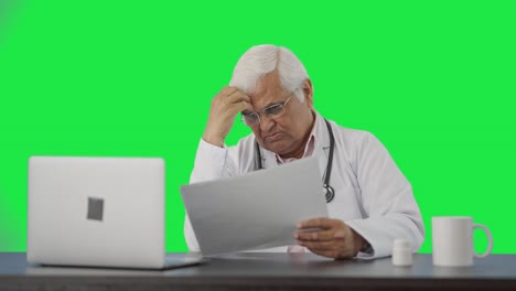 Confused-Indian-senior-doctor-reading-health-reports-Green-screen