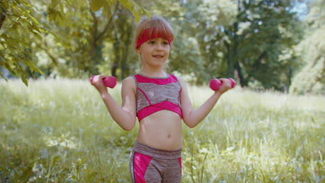 Athletic-young-sporty-fit-child-kid-girl-working-out-dumbbells-in-park-performing-bicep-exercising