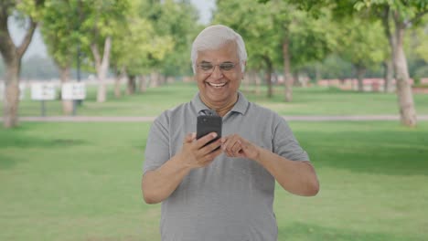 Happy-Indian-old-man-scrolling-through-phone-in-park