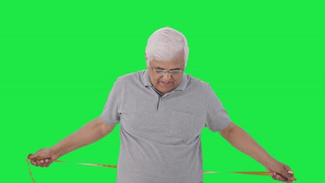 Sad-Indian-old-man-checking-his-waist-size-using-inch-tape-Green-screen