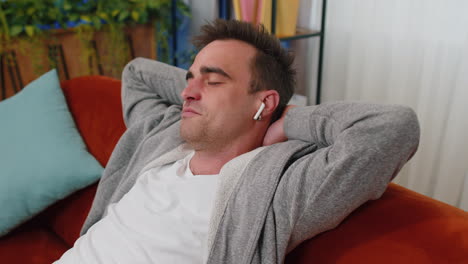 Man-in-wireless-earphones-listening-favorite-disco-music-relaxing-sleeping-resting-on-couch-at-home