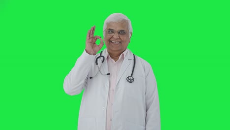 Happy-Indian-senior-doctor-showing-okay-sign-Green-screen