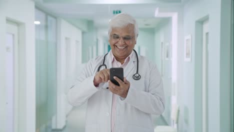 Feliz-Médico-Senior-Indio-Desplazándose-Por-El-Teléfono