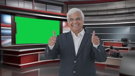 Happy-Indian-senior-journalist-pointing-at-green-screen-and-showing-thumbs-up