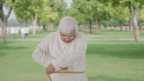 Indian-old-man-measuring-waist-using-inch-tape-in-park