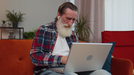 Senior-grandfather-man-freelancer-working-on-laptop,-sends-messages,-makes-online-purchases-at-home