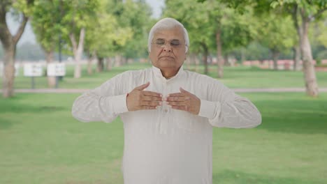 Indian-old-man-doing-breathe-in-breathe-out-exercise-in-park