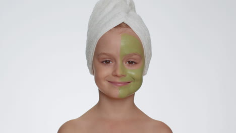 Lovely-smiling-child-girl-kid-in-towel-on-head-applying-cleansing-moisturizing-green-mask-on-face