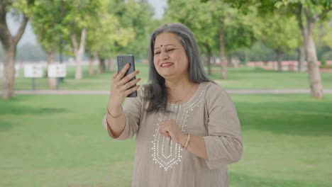 Happy-Indian-old-woman-talking-on-video-call-in-park